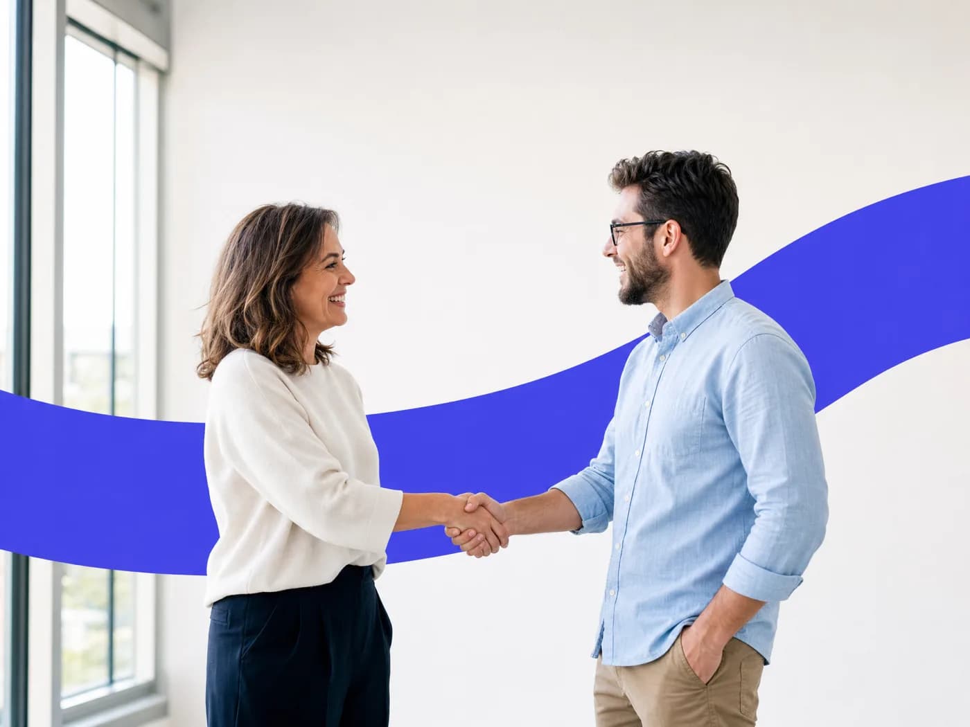 Two professionals smiling as they shake hands in a bright office