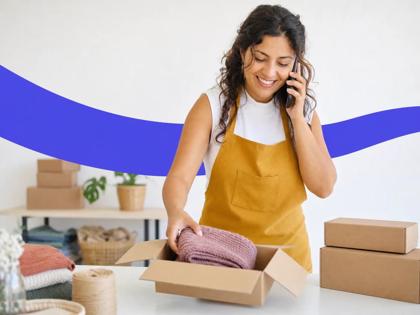 A shop owner on the phone smiling as she packs a knitted scarf into a parcel