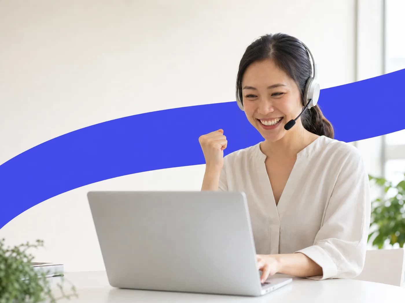 A saleswoman on a headset smiling and making a small happy fist at her laptop