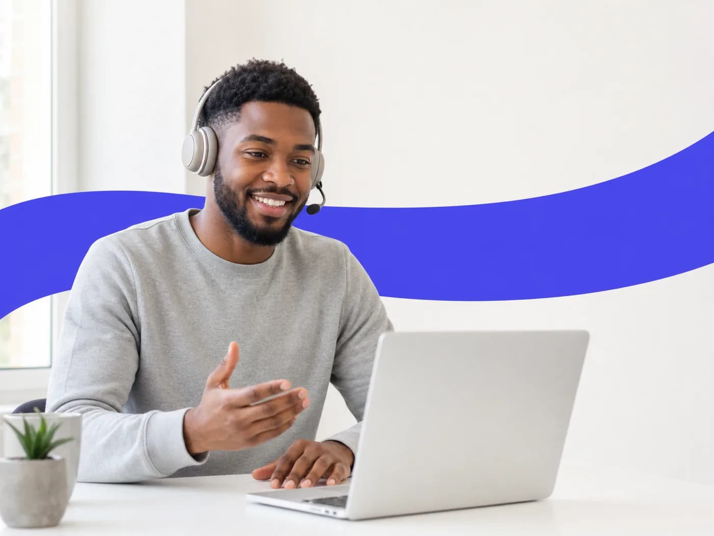 A support agent on a headset smiling as he talks a customer through a fix at his laptop