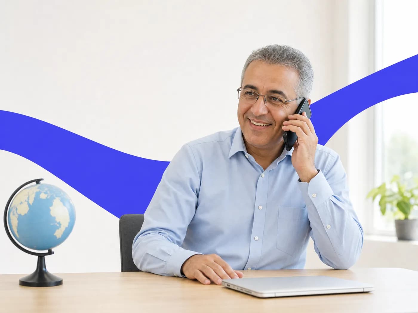 A travel agent smiling on a phone call at his desk beside a small globe
