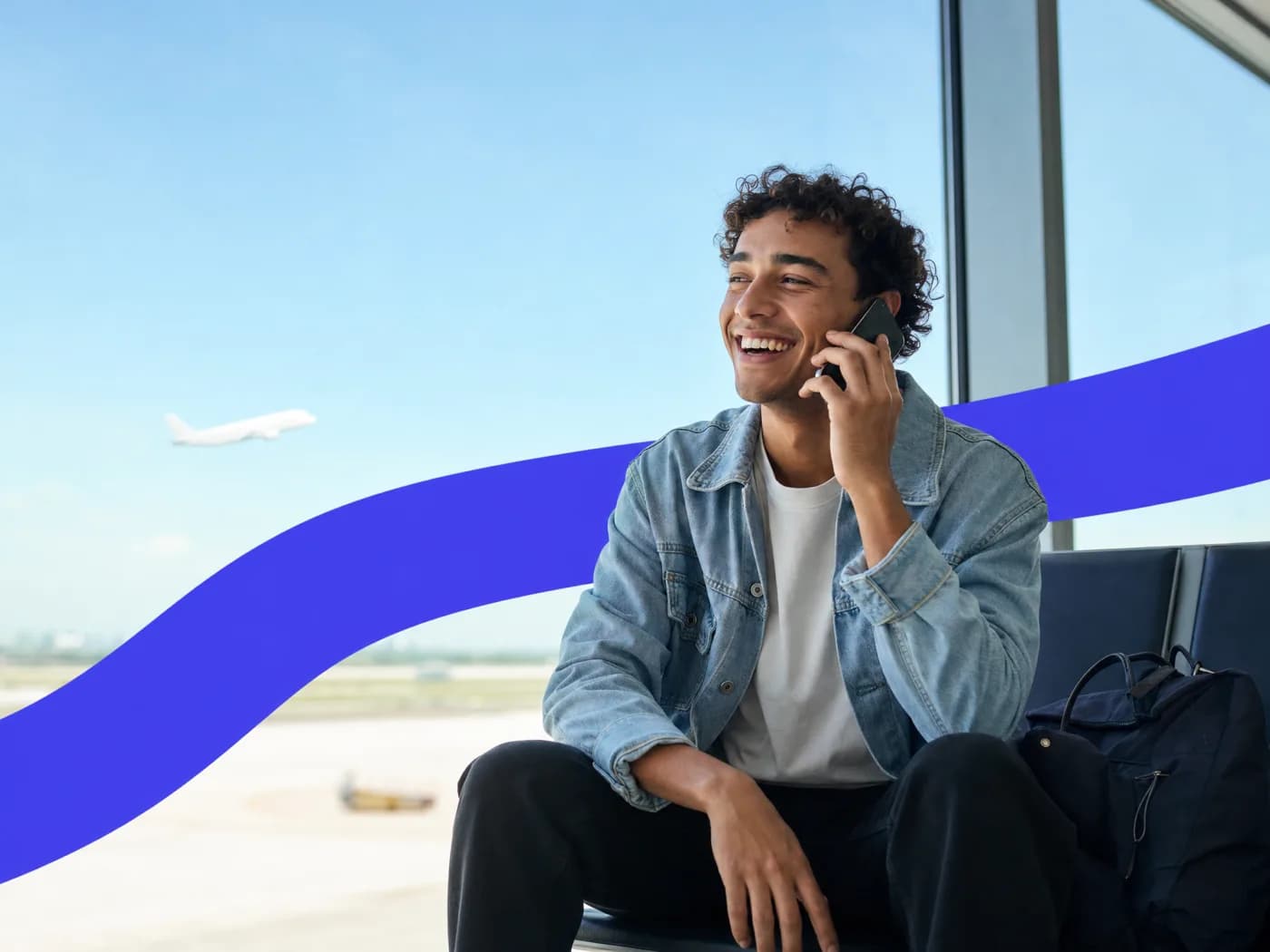 A young man laughing on a phone call in a sunny airport lounge